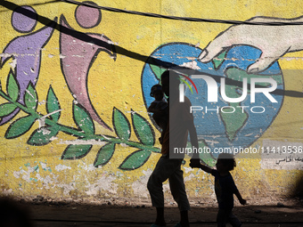 A man is walking with his children past a mural painted on the wall of the UN school sheltering displaced people, following an Israeli strik...