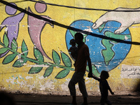 A man is walking with his children past a mural painted on the wall of the UN school sheltering displaced people, following an Israeli strik...