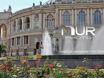 A woman is taking a picture of the fountain near the Odesa National Academic Opera and Ballet Theatre on a hot summer day in Odesa, Ukraine,...