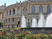 A woman is taking a picture of the fountain near the Odesa National Academic Opera and Ballet Theatre on a hot summer day in Odesa, Ukraine,...