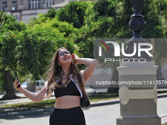 A smiling woman is holding a smartphone on a hot summer day in Odesa, Ukraine, on July 13, 2024. NO USE RUSSIA. NO USE BELARUS. (