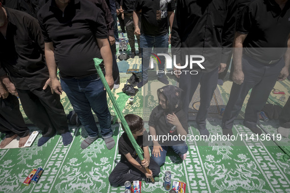 Two children are sitting together while Iraqi men living in Iran are praying during a religious festival to commemorate Ashura, in Dolatabad...