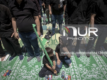 Two children are sitting together while Iraqi men living in Iran are praying during a religious festival to commemorate Ashura, in Dolatabad...