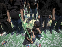 Two children are sitting together while Iraqi men living in Iran are praying during a religious festival to commemorate Ashura, in Dolatabad...