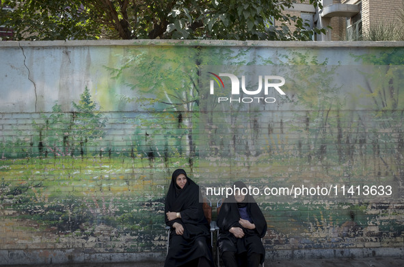 Two veiled women are sitting on a sidewalk during a religious festival to commemorate Ashura, in Dolatabad neighborhood in southern Tehran,...