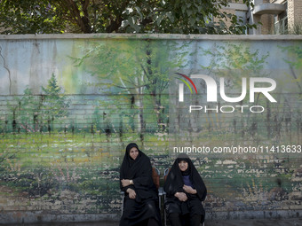 Two veiled women are sitting on a sidewalk during a religious festival to commemorate Ashura, in Dolatabad neighborhood in southern Tehran,...