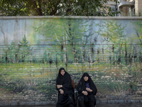 Two veiled women are sitting on a sidewalk during a religious festival to commemorate Ashura, in Dolatabad neighborhood in southern Tehran,...