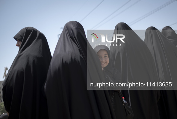 A young veiled girl is looking on while standing next to her mother during a religious festival to commemorate Ashura, in Dolatabad neighbor...