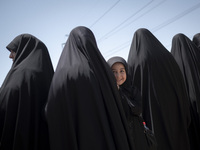 A young veiled girl is looking on while standing next to her mother during a religious festival to commemorate Ashura, in Dolatabad neighbor...