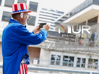 A man dressed as Uncle Sam, wearing a bandage on his ear reading 'fight fight fight' takes a photograph of protestors at Red Arrow Park in M...