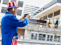 A man dressed as Uncle Sam, wearing a bandage on his ear reading 'fight fight fight' takes a photograph of protestors at Red Arrow Park in M...