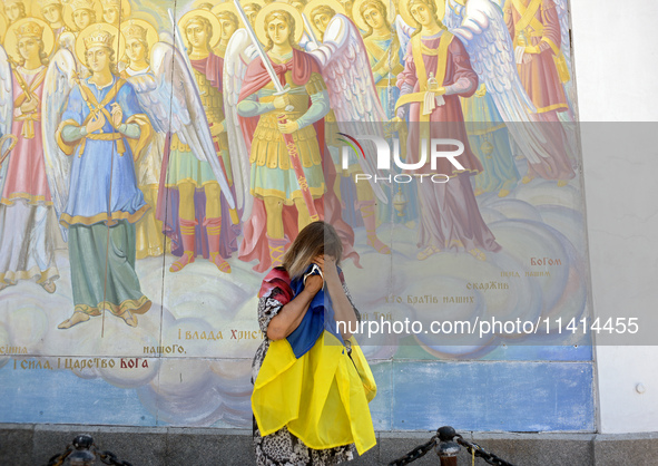 A woman with a Ukrainian flag is crying at a fresco of the St. Michael's Golden-Domed Monastery hosting the memorial service of the commande...