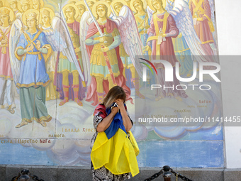 A woman with a Ukrainian flag is crying at a fresco of the St. Michael's Golden-Domed Monastery hosting the memorial service of the commande...