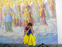 A woman with a Ukrainian flag is crying at a fresco of the St. Michael's Golden-Domed Monastery hosting the memorial service of the commande...