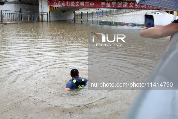 Law enforcement officers of Shizhong District Comprehensive Administrative Law Enforcement Bureau are wading through a waterlogged road in Z...