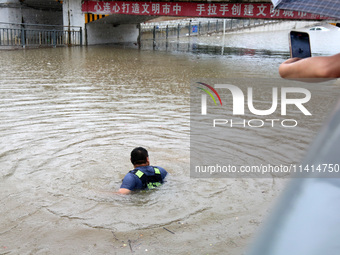 Law enforcement officers of Shizhong District Comprehensive Administrative Law Enforcement Bureau are wading through a waterlogged road in Z...