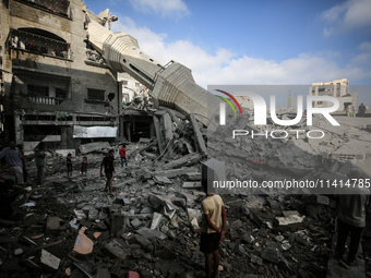 Palestinians are standing on the rubble of Abdullah Azzam Mosque, destroyed in Israeli bombardment in Nuseirat, central Gaza Strip, on July...