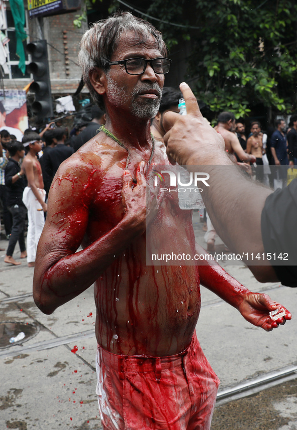 A volunteer is sprinkling rose water on the wounds of a Shi'ite Muslim after he flagellates himself during a Muharram procession marking Ash...