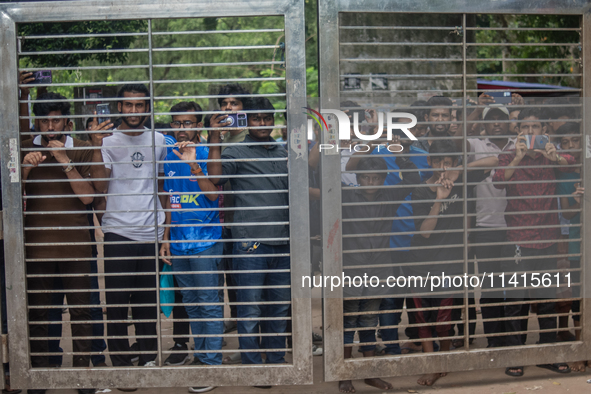 Curious people are gathering as they are standing behind a gate near the University of Dhaka as police are firing teargas during a coffin ra...