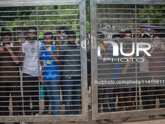 Curious people are gathering as they are standing behind a gate near the University of Dhaka as police are firing teargas during a coffin ra...