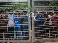 Curious people are gathering as they are standing behind a gate near the University of Dhaka as police are firing teargas during a coffin ra...