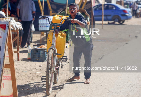 A boy is pushing a bicycle loaded with two jerrycans on the handlebars after filling up from a desalination plant in Deir el-Balah in the ce...