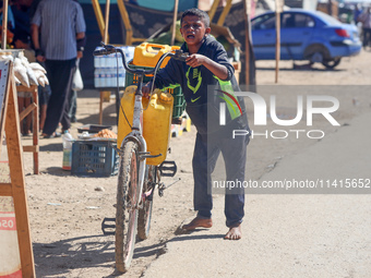 A boy is pushing a bicycle loaded with two jerrycans on the handlebars after filling up from a desalination plant in Deir el-Balah in the ce...