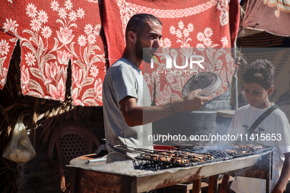 A Palestinian man is preparing grilled meat next to a temporary camp in Deir el-Balah, in the central Gaza Strip, on July 17, 2024, amid the...