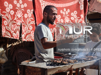 A Palestinian man is preparing grilled meat next to a temporary camp in Deir el-Balah, in the central Gaza Strip, on July 17, 2024, amid the...