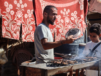 A Palestinian man is preparing grilled meat next to a temporary camp in Deir el-Balah, in the central Gaza Strip, on July 17, 2024, amid the...