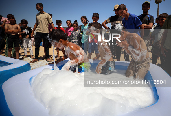 Displaced Palestinian children are playing together in the water in swimming pools in a makeshift camp during hot weather in Deir el-Balah,...