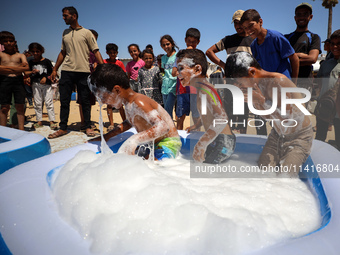 Displaced Palestinian children are playing together in the water in swimming pools in a makeshift camp during hot weather in Deir el-Balah,...