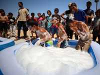 Displaced Palestinian children are playing together in the water in swimming pools in a makeshift camp during hot weather in Deir el-Balah,...