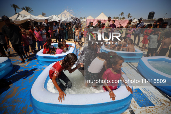 Displaced Palestinian children are playing together in the water in swimming pools in a makeshift camp during hot weather in Deir el-Balah,...