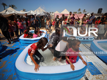 Displaced Palestinian children are playing together in the water in swimming pools in a makeshift camp during hot weather in Deir el-Balah,...