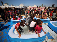 Displaced Palestinian children are playing together in the water in swimming pools in a makeshift camp during hot weather in Deir el-Balah,...