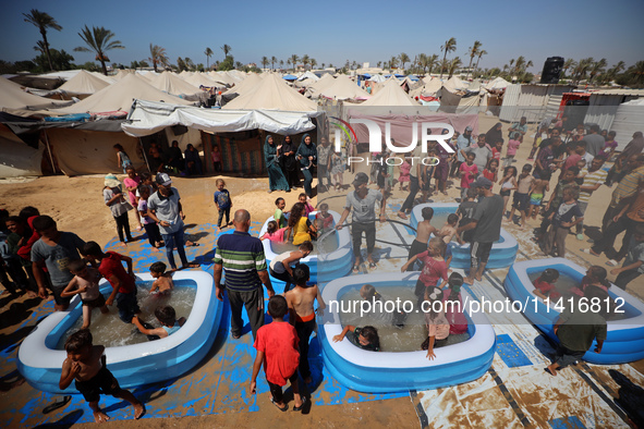 Displaced Palestinian children are playing together in the water in swimming pools in a makeshift camp during hot weather in Deir el-Balah,...