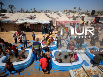 Displaced Palestinian children are playing together in the water in swimming pools in a makeshift camp during hot weather in Deir el-Balah,...