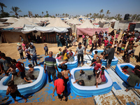 Displaced Palestinian children are playing together in the water in swimming pools in a makeshift camp during hot weather in Deir el-Balah,...