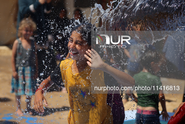 Displaced Palestinian children are playing together in the water in swimming pools in a makeshift camp during hot weather in Deir el-Balah,...