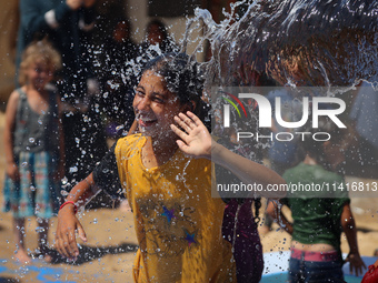 Displaced Palestinian children are playing together in the water in swimming pools in a makeshift camp during hot weather in Deir el-Balah,...