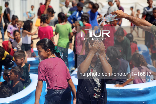 Displaced Palestinian children are playing together in the water in swimming pools in a makeshift camp during hot weather in Deir el-Balah,...