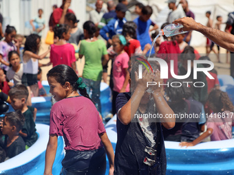 Displaced Palestinian children are playing together in the water in swimming pools in a makeshift camp during hot weather in Deir el-Balah,...