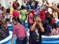 Displaced Palestinian children are playing together in the water in swimming pools in a makeshift camp during hot weather in Deir el-Balah,...