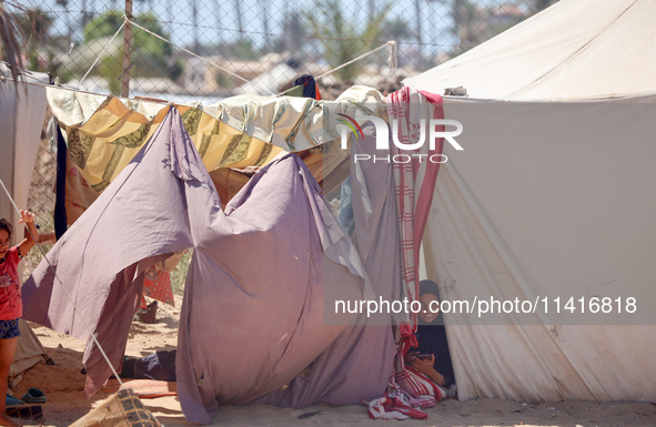 Displaced Palestinian children are playing together in the water in swimming pools in a makeshift camp during hot weather in Deir el-Balah,...