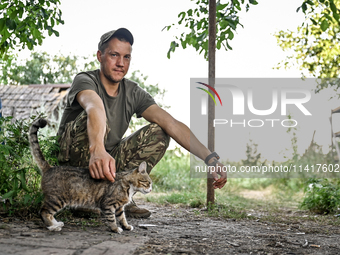 A serviceman of the 24th King Danylo Separate Mechanized Brigade, who goes by the call sign of Myron, is petting a cat at combat positions n...