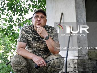 Andrii, a commander of an artillery crew of the 24th King Danylo Separate Mechanized Brigade, is holding a handheld transceiver while squatt...