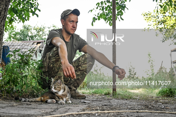 A serviceman of the 24th King Danylo Separate Mechanized Brigade, who goes by the call sign of Myron, is petting a cat at combat positions n...