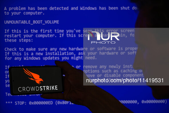 The CrowdStrike logo is being displayed on a smartphone with a Windows blue screen visible in the background in this photo illustration in B...