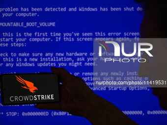 The CrowdStrike logo is being displayed on a smartphone with a Windows blue screen visible in the background in this photo illustration in B...